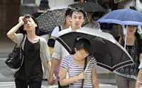 厳しい暑さの東京・銀座で、日傘を差したり汗をふきながら歩く人たち（17日）=共同
