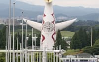 今も万博記念公園に残る太陽の塔。左手前は万博当時各国・地域の旗を掲げたポール