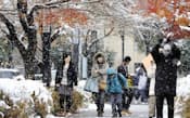 雪で白く染まった名古屋市内を歩く人たち（26日）=共同
