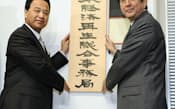 日本経済再生本部の事務局に看板を掛ける安倍首相(右)と甘利経済再生相=7日午前、内閣府