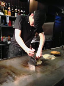 2本のへらを操りお好み焼きを押さえつける。押さえつけることでキャベツや麺など具材が一体化する。