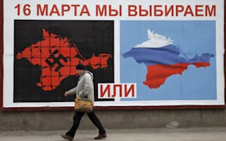 16日、ウクライナ南部クリミア半島セバストポリで、住民投票参加を呼び掛けるポスターの前を歩く男性=ロイター