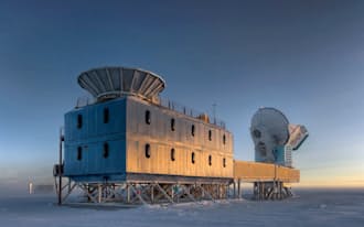 BICEP2望遠鏡は南極点から約800m離れた場所にある。写真は米アムンゼン・スコット基地のダークセクター実験棟と呼ばれる建物で,BICEP2は手前の建物の屋上,おわん形のシールドの中に置かれている。画面奥に見えるのは同じく原始重力波を探索している南極点望遠鏡(画像はSteffen Richter、　Harvard University提供)