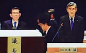 27日の株主総会では厳しい声を浴びた（森会長(左)と八木社長）=モニター画面