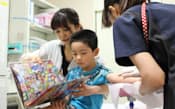 治療室で男児に採血をする看護師と、絵本を読む子ども療養支援士（宮城県立こども病院）
