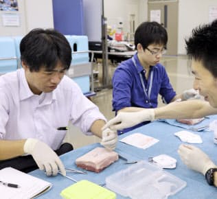 研修医（中央）と並んで豚の皮を使った皮膚縫合を体験する記者(左)（９月16日、横浜市立大病院）
