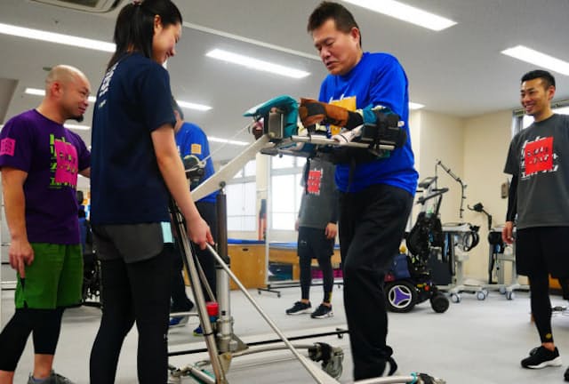 トレーナーらの補助のもと、専用の歩行器を使ってジムの中を歩く上野さん（東京・江東）
