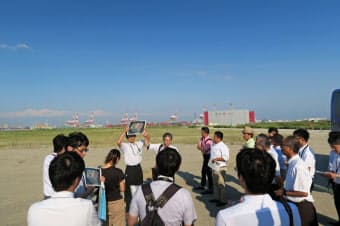 夢洲を視察する万博基本構想検討委員会のメンバー。後方にコンテナターミナルのクレーンが立ち並ぶ