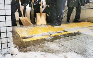 転倒防止のため、地下につながる出入り口で雪かきをする駅職員（24日、東京都杉並区）
