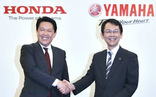 二輪車の生産、開発の提携を発表し、握手するホンダの青山真二取締役(左)とヤマハ発動機の渡部克明取締役（10月、東京都港区）