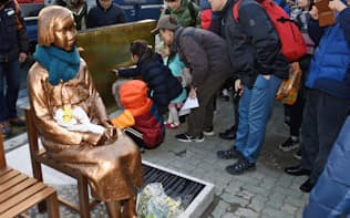 韓国・釜山の日本総領事館前の歩道に少女像が設置され、銘板に足を止める市民ら=共同