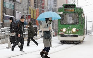 雪の中、札幌市の中心部を歩く人たち（12日）=共同