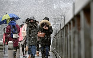 雪が降る中、京都・嵐山の渡月橋を渡る観光客ら（14日午後）=共同