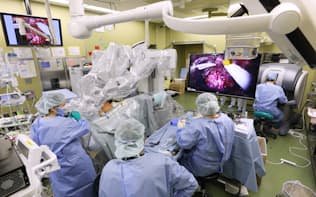 右奥で医師が手術支援ロボット「ダヴィンチ」のアーム（左手前）を操り、患者の前立腺がんを摘出する（東京・新宿の東京医大病院）