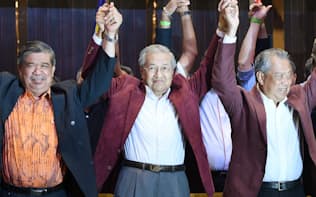 記者会見で手を取り合って喜ぶマハティール元マレーシア首相(中)（10日未明、クアラルンプール郊外）=柏原敬樹撮影