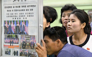 平壌の地下鉄駅構内に掲示された米朝首脳会談を報じる朝鮮労働党機関紙の労働新聞を見る市民ら(13日)=共同 平壌の地下鉄駅構内に掲示された米朝首脳会談を報じる朝鮮労働党機関紙の労働新聞を見る市民ら(13日)=共同