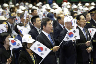 25日、ソウルで、朝鮮戦争開戦から68年の式典で韓国国旗を振る同国の李洛淵首相(中央)=AP 25日、ソウルで、朝鮮戦争開戦から68年の式典で韓国国旗を振る同国の李洛淵首相(中央)=AP