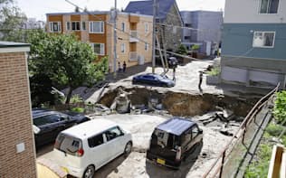 地震で陥没した道路と泥に埋まった乗用車（6日午前、札幌市清田区）=共同