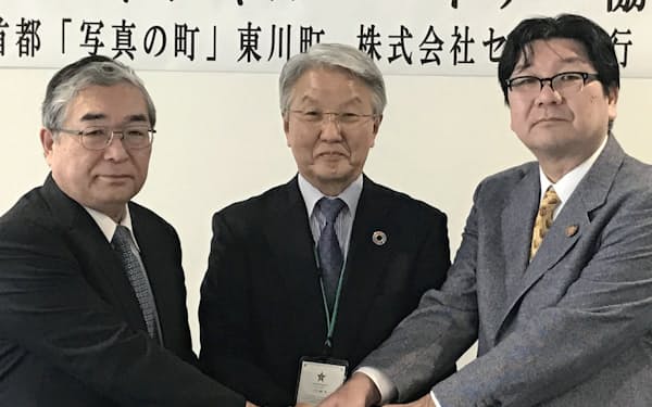 締結式で握手する東川町の松岡町長(左)、セブン銀の二子石会長(中)ら