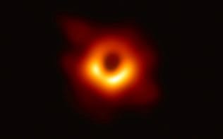M87銀河の中心にある巨大ブラックホールを撮影した画像。中心の黒い部分がブラックホールの影（EHTコラボレーション提供）
