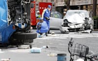 歩行者が巻き込まれた事故現場で乗用車（奥）を調べる警察官（19日、東京都豊島区）