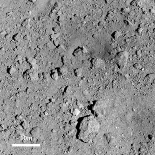 人工クレーター付近の様子(高度約500メートルから撮影。中央右上の色が暗くくぼんだ場所がクレーター)=JAXAなど提供 人工クレーター付近の様子(高度約500メートルから撮影。中央右上の色が暗くくぼんだ場所がクレーター)=JAXAなど提供