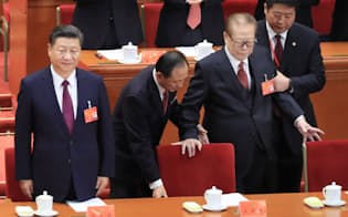 共産党大会に臨む習近平総書記(左)と体を支えられながら席に着く江沢民元国家主席（右から2人目）（2017年10月18日、北京の人民大会堂）=小高顕撮影