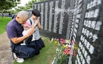 「慰霊の日」を迎え、沖縄戦犠牲者の名前が刻まれた「平和の礎（いしじ）」の前で手を合わせる遺族（23日午前、沖縄県糸満市の平和祈念公園）