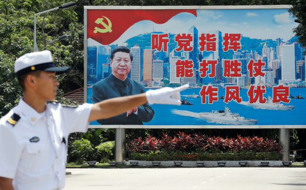 習国家主席の看板の前に立つ中国人民解放軍の兵士(2019年6月30日、香港)=ロイター 習国家主席の看板の前に立つ中国人民解放軍の兵士(2019年6月30日、香港)=ロイター
