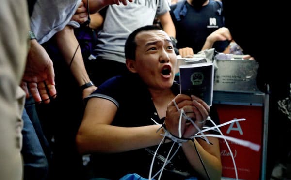 デモ隊の一部に拘束された中国共産党系の環球時報の記者(13日、香港国際空港)=ロイター