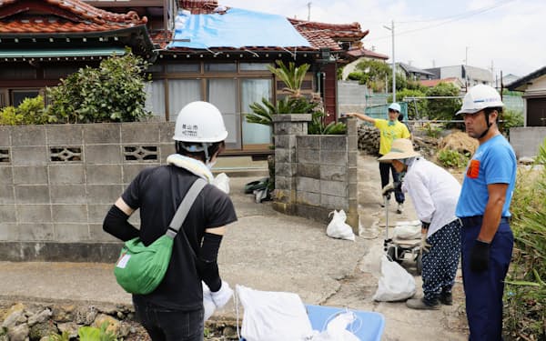 屋根に張るブルーシートを押さえる土のうを運ぶボランティアら(14日午前、千葉県館山市)=共同