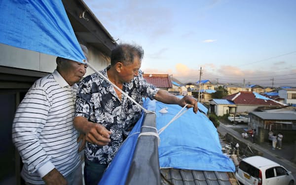 　台風17号から変わった温帯低気圧による強風に備え、張っていたブルーシートの一部を撤去する住民の男性ら（23日午後、千葉県鋸南町）=共同