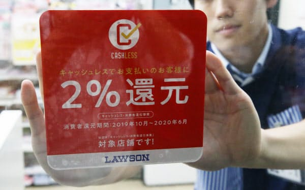 キャッシュレス決済で2%還元を知らせるステッカーを貼るコンビニの店員(10月1日、東京都内)