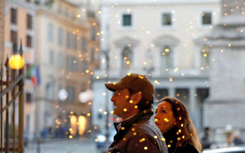 クリスマスの飾り付けで光るショーウインドーの前を歩くふたり(11日、ローマ)=ロイター クリスマスの飾り付けで光るショーウインドーの前を歩くふたり(11日、ローマ)=ロイター
