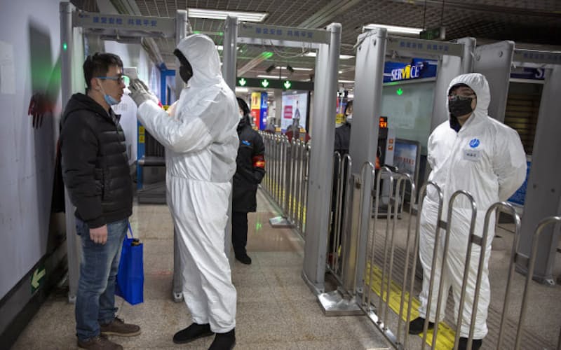 北京市内の地下鉄駅で乗客の体温を測る防護服姿の係員(26日)=AP 北京市内の地下鉄駅で乗客の体温を測る防護服姿の係員(26日)=AP