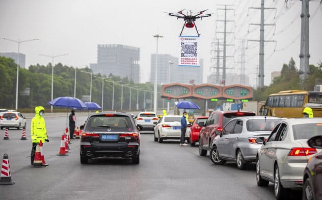 広東省深圳市では市内に入る車両の運転手は、その入口となる高速道路の料金所でドローンがぶら下げているQRコードを自分のスマホで読み取り、登録しなければならない=AP 広東省深圳市では市内に入る車両の運転手は、その入口となる高速道路の料金所でドローンがぶら下げているQRコードを自分のスマホで読み取り、登録しなければならない=AP