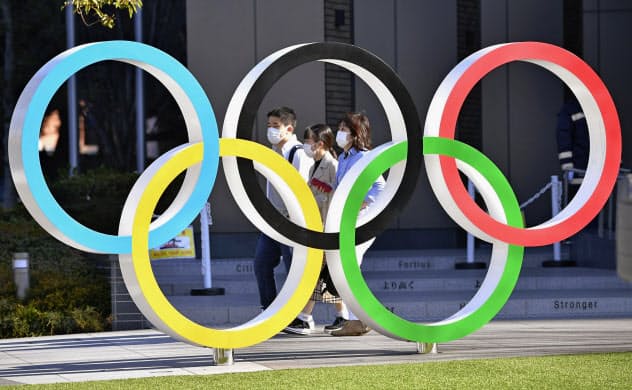五輪マークのモニュメントの後ろをマスク姿で歩く人たち(12日午後、東京都新宿区)=共同 五輪マークのモニュメントの後ろをマスク姿で歩く人たち(12日午後、東京都新宿区)=共同