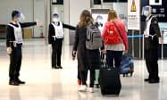 顔を覆う透明なフェースシールドとマスクを着用し、旅客(後ろ姿)を誘導する成田空港検疫所の関係者。海外から帰国した人の感染判明が増えている(21日)=共同 顔を覆う透明なフェースシールドとマスクを着用し、旅客(後ろ姿)を誘導する成田空港検疫所の関係者。海外から帰国した人の感染判明が増えている(21日)=共同