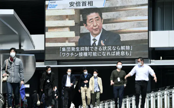 緊急事態宣言の発令についてのニュースが流れる街頭モニター(8日午前、東京都千代田区)=中岡詩保子撮影