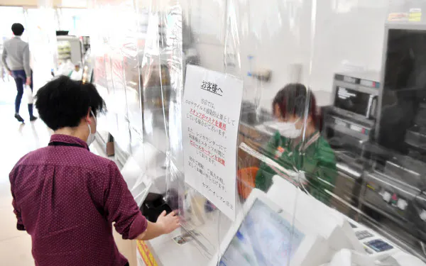 感染防止のため、透明な仕切り越しに接客するコンビニエンスストアの従業員(8日、東京都港区のセブンイレブン芝浦4丁目店)=野岡香里那撮影