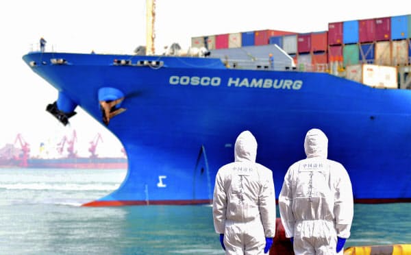 コンテナ船のそばに立つ、防護服を着た労働者(3月31日、中国・山東省)=Chinatopix・AP