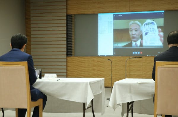 マスクや消毒液、防護服などのメーカートップらとテレビ会議で話す安倍首相(手前左)=15日、首相官邸