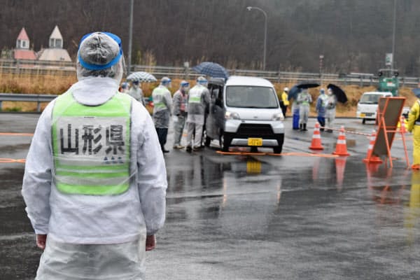 フェースシールドなどをつけた県職員がドライバーに検温に協力を呼びかける(18日、山形市の山形蔵王パーキングエリア)