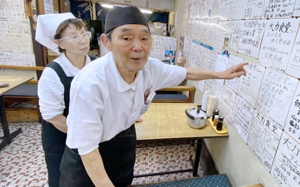 来店した高校球児らが描いた色紙を指しながら思い出を語る大力食堂店主の藤坂悦夫さん（81）(右)と妻の初枝さん（78）（18日、兵庫県西宮市）