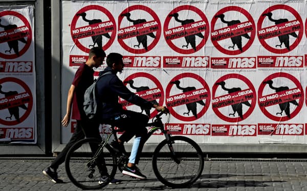 「債務返済にノー」と書かれたポスターの前を歩くブエノスアイレス市民=ロイター
