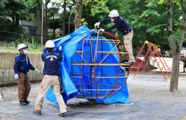 遊具に巻かれたブルーシートをはがす関係者(26日午前、東京都目黒区の駒沢公園)