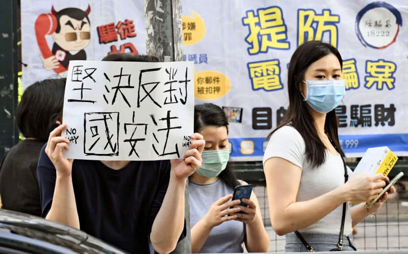 6月28日、デモ行進が行われた香港・九竜地区で「国家安全法に断固反対」と書かれた紙を掲げる人=共同 6月28日、デモ行進が行われた香港・九竜地区で「国家安全法に断固反対」と書かれた紙を掲げる人=共同