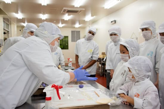 「こども参観」でお菓子づくりの説明を受ける従業員の子どもたち(2019年8月、近江八幡工場)