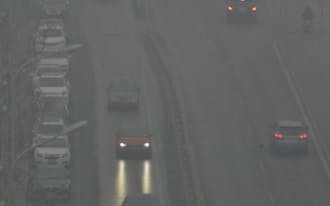 大気汚染が悪化し濃霧につつまれた北京市内で29日、日中にライトをつけて走る車=共同