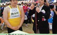 約30年前、丸井の運動会で開かれた腕相撲大会で優勝し、青井忠雄社長（現・名誉会長）からたたえられる小田桐英裕さん（現・立川談笑師匠）。当時の社内報より抜粋=丸井グループ提供